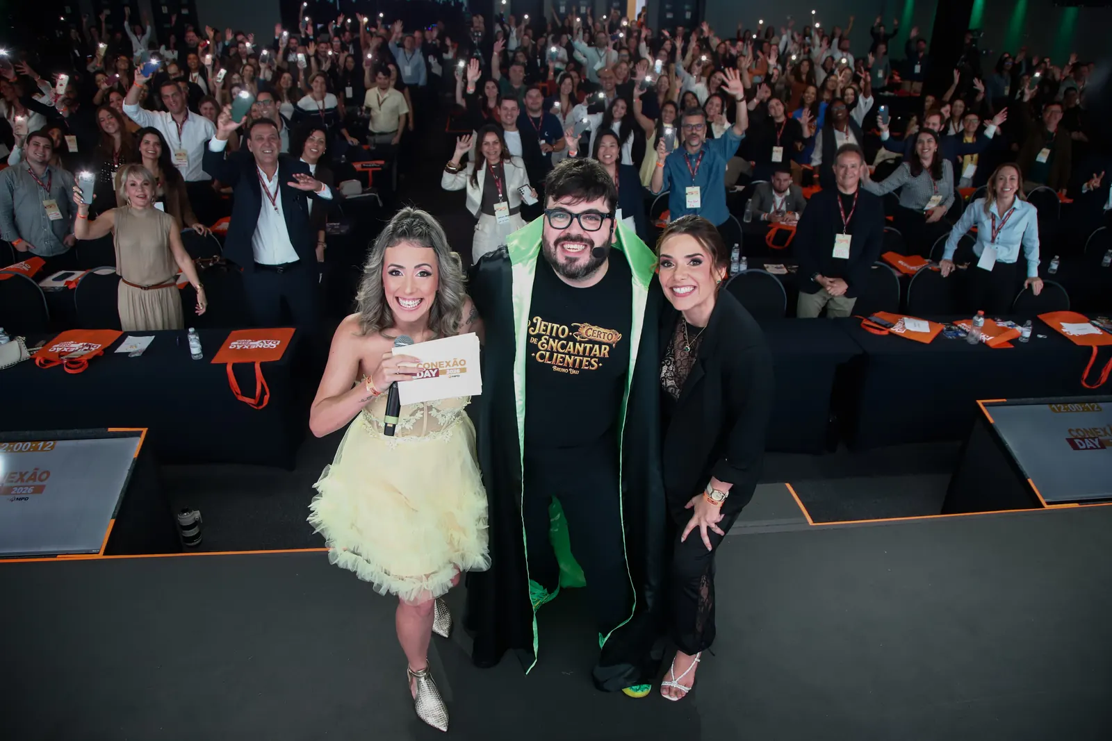 Foto final do Conexão Day: o Bruno UAU no palco, com a plateia inteira atrás acenando