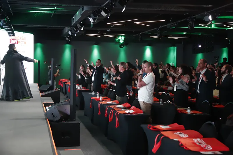 Plateia do Conexão Day de pé, de braços para cima, com o Bruno UAU no palco