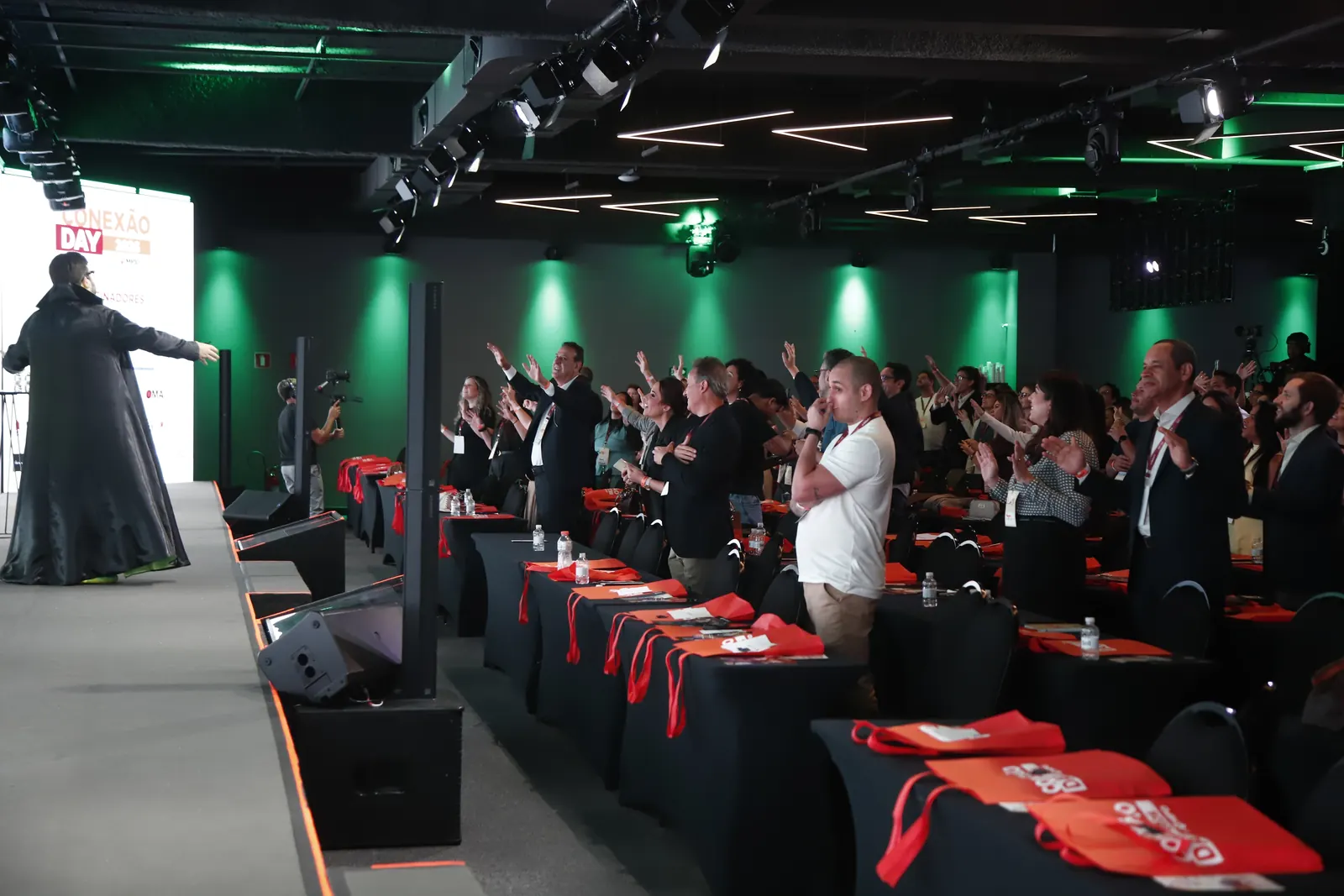 Plateia do Conexão Day de pé, de braços para cima, com o Bruno UAU no palco