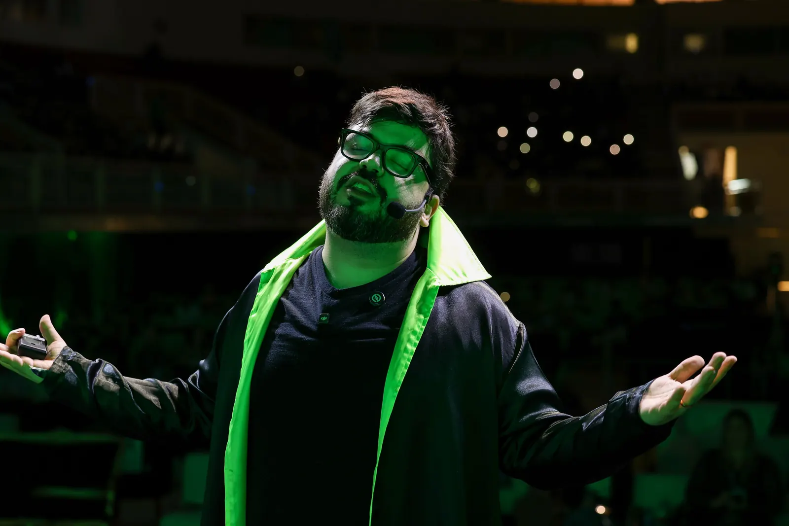 Bruno UAU de olhos fechados e braços abertos, com a arena escura ao fundo