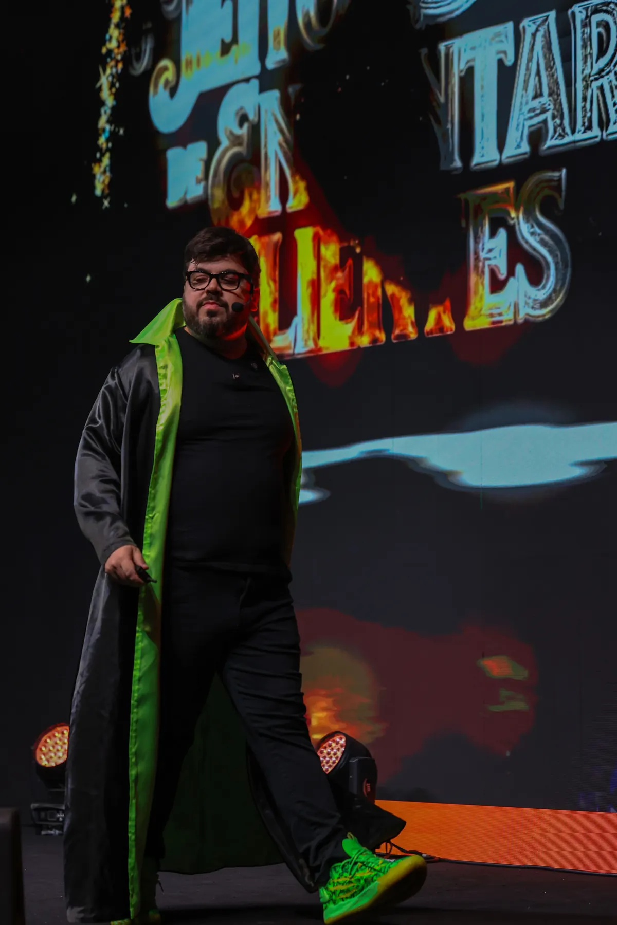 Bruno UAU andando no palco, de tênis verdes, diante do logo da palestra no telão